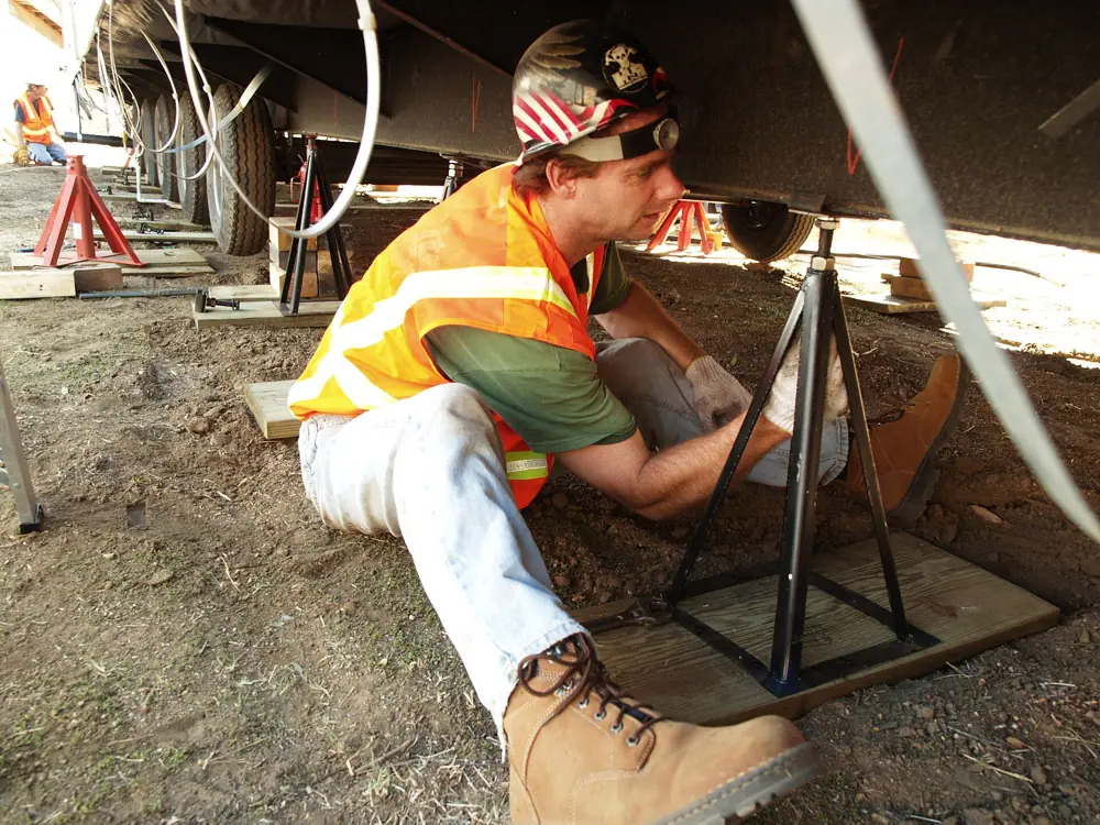 A worker setting a steel pier stand under a manufactured home