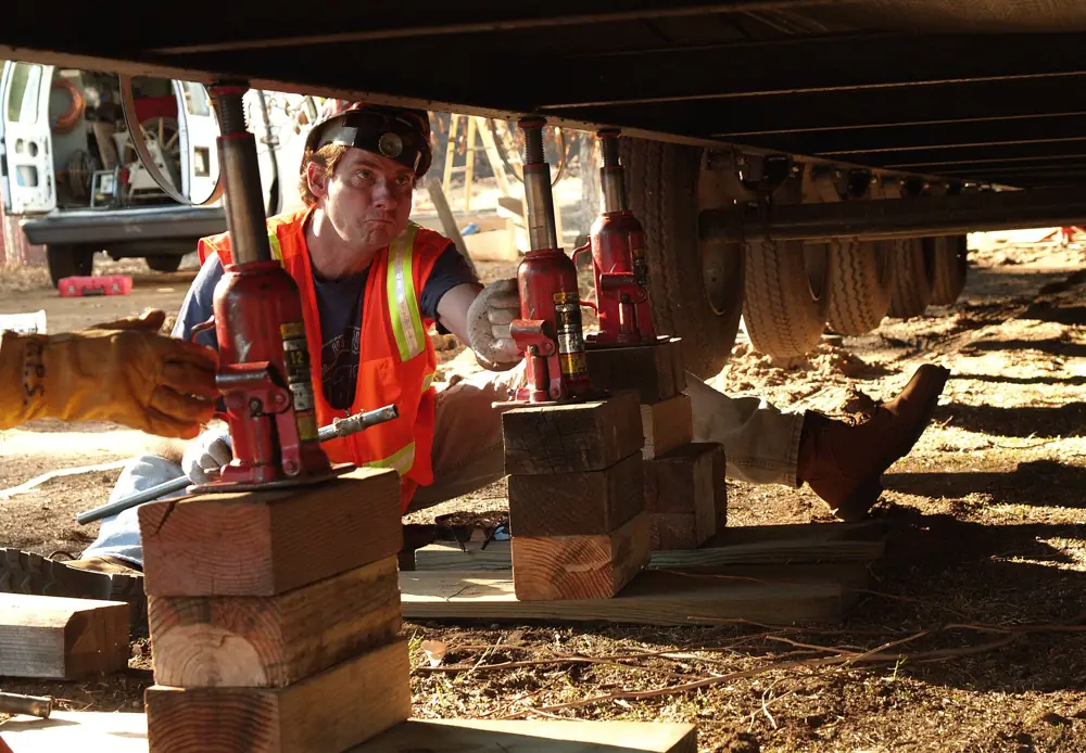 A worker stacking concrete block piers under a mobile home